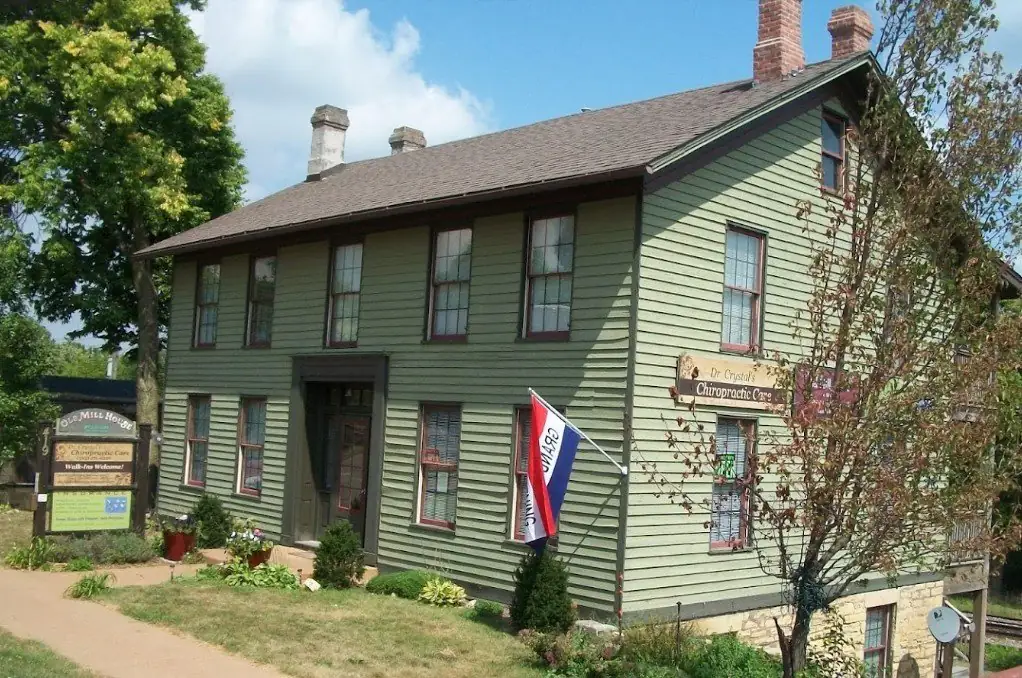 Dr. Crystal's Chiropractic Care clinic at the historic Old Mill House, 419 N. Cody Road, Le Claire Iowa — a charming sage-green two-story building with clinic sign and garden.